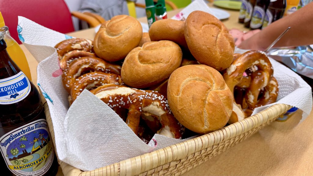 Korb mit frischen Brezn und Semmeln neben einer Flasche alkoholfreiem Bier.